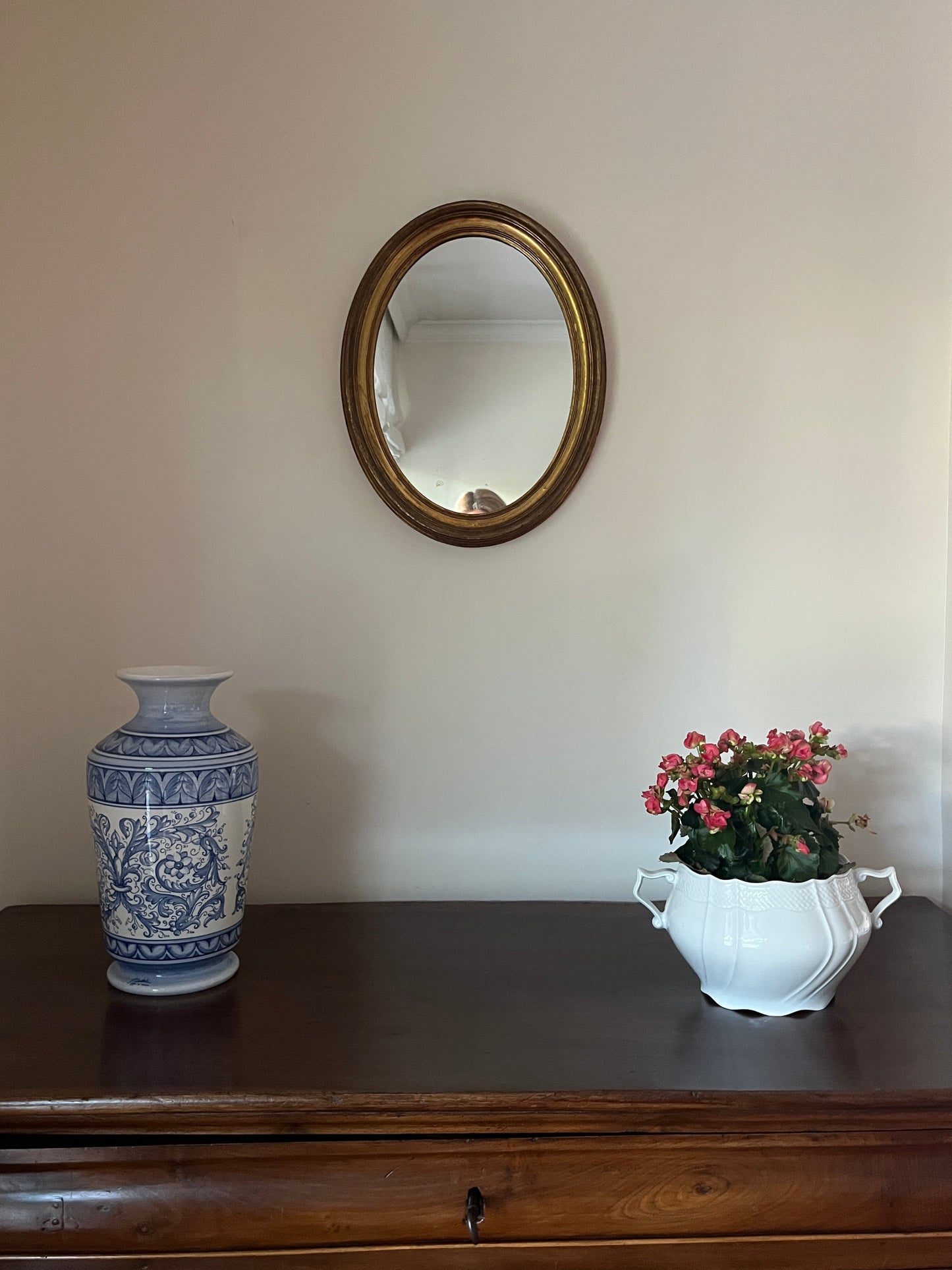 Oval mirror on a wall next to a vase and a decorative item.