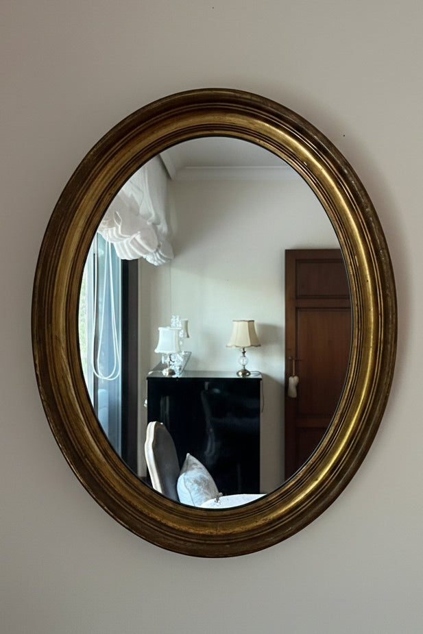 Oval gold-framed mirror on a white wall