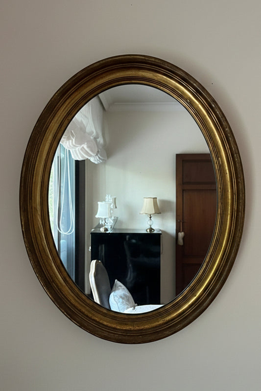 Oval gold-framed mirror on a white wall